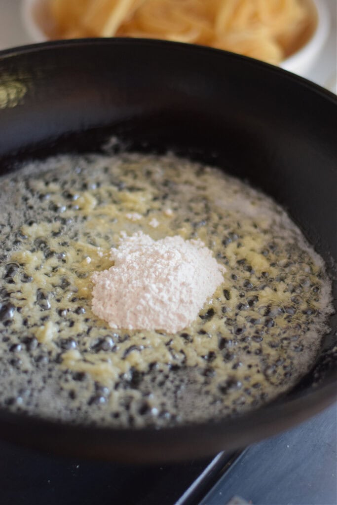 Adding flour to butter and garlic in a skillet.