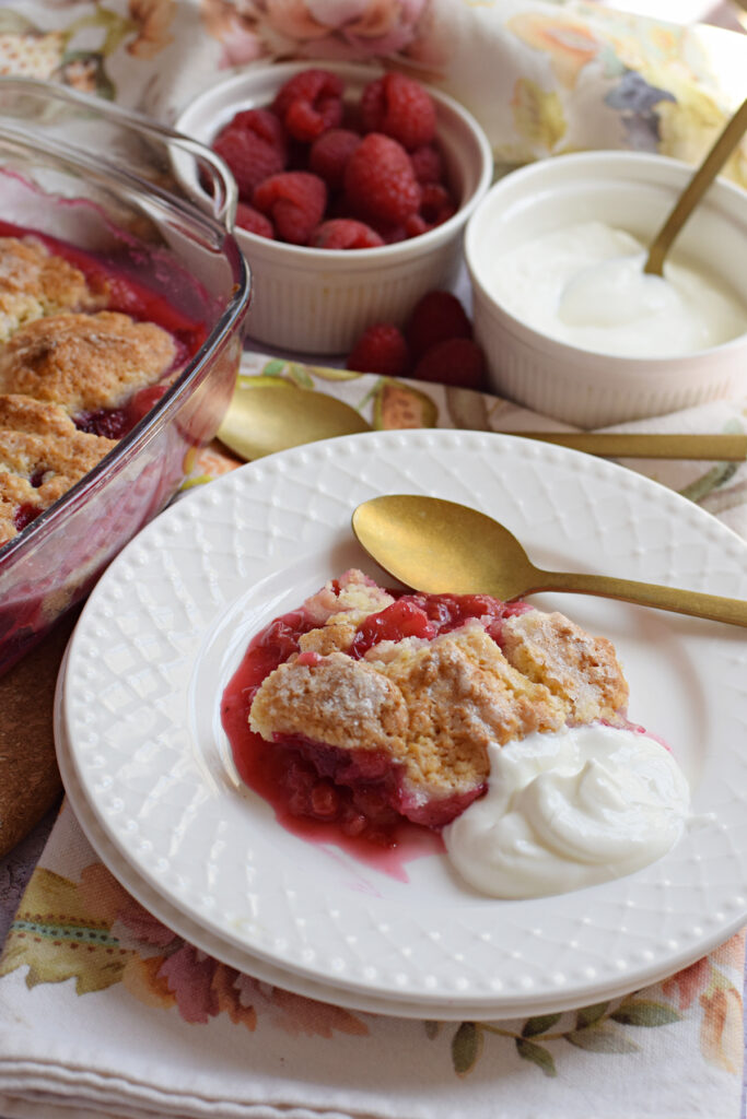 Raspberry cobbler on a plate with whipped cream.
