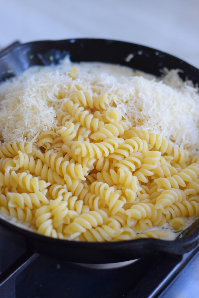 Adding pasta spirals and cheese to a skillet.