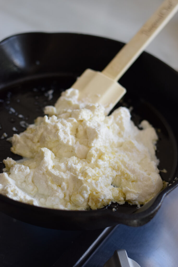Adding ricotta cheese to a skillet.