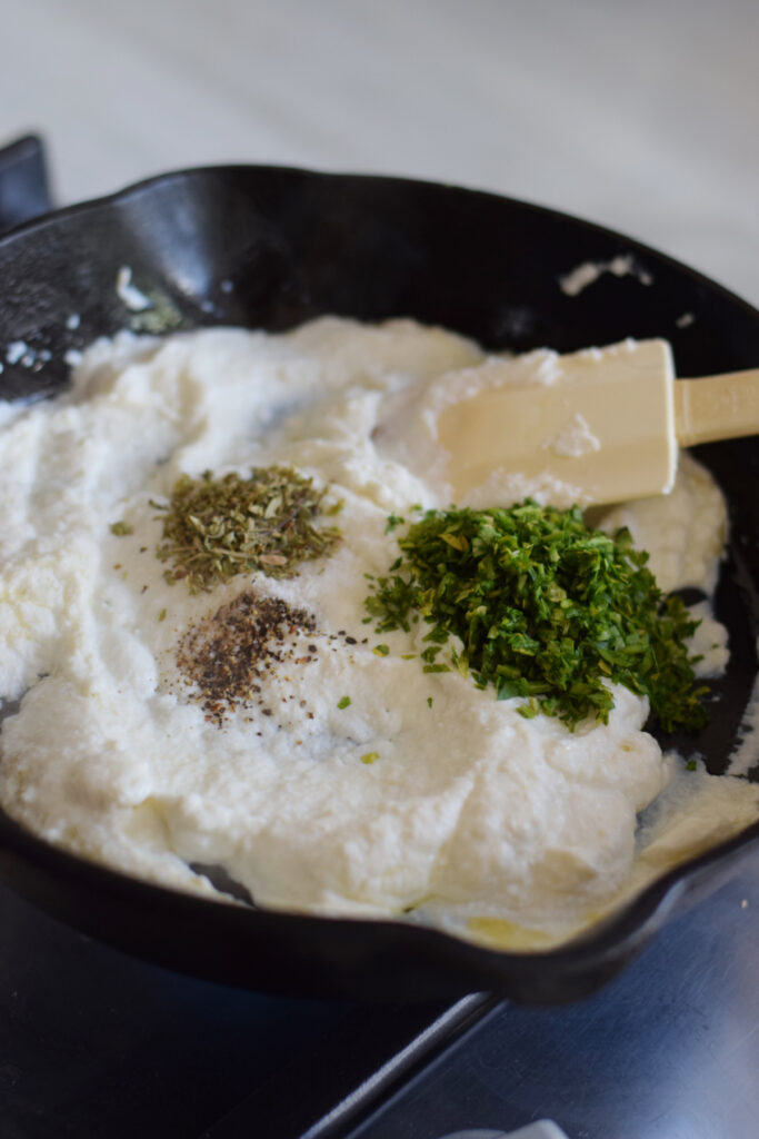 Adding seasonings to a skillet with ricotta cheese.