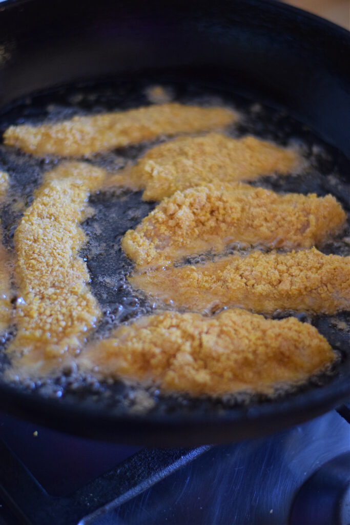 Cooking breaded chicken strips in oil in a skillet.