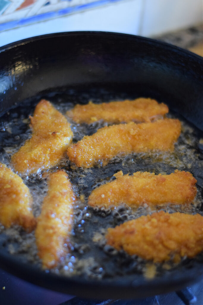 Cooking breaded chicken strips in a skillet.