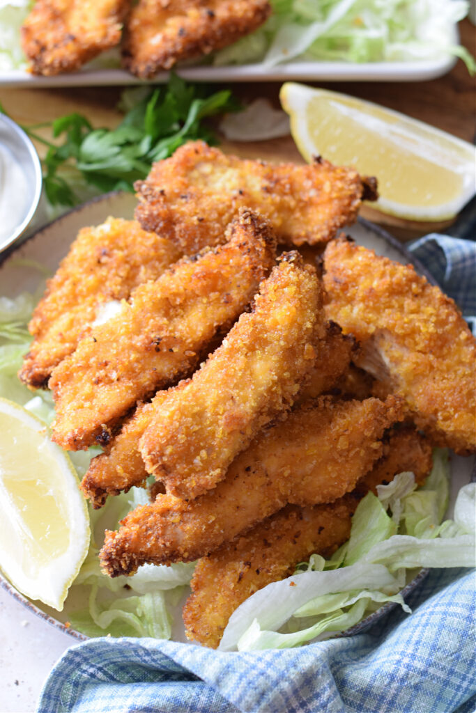 Chicken strips on a plate with lettuce and lemon wedges.