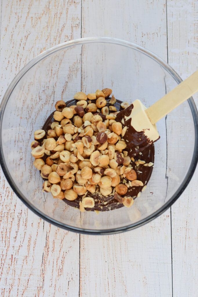 Hazelnuts and melted chocolate in a glass bowl.