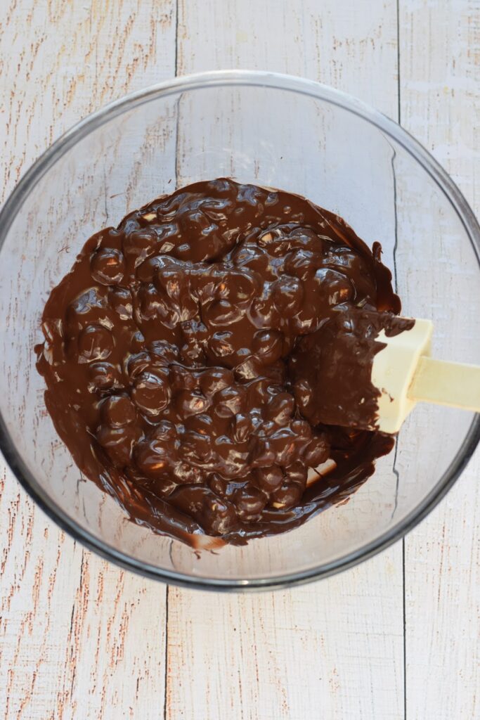Hazelnuts and melted chocolate in a glass bowl.
