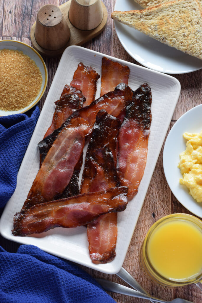 Baked bacon with brown sugar on a white serving plate.