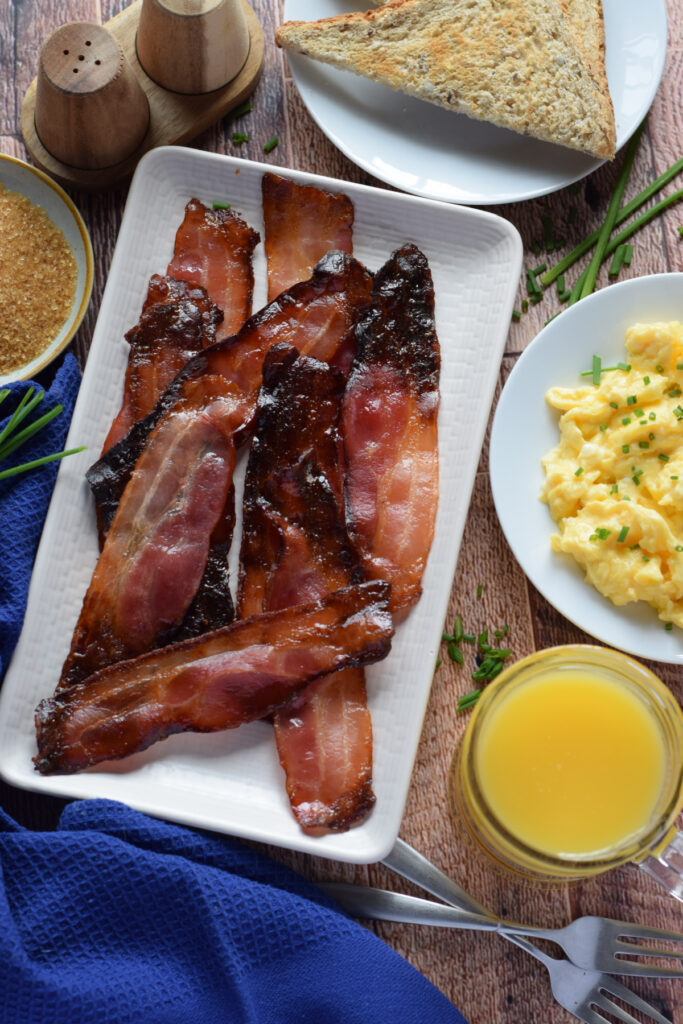 Bacon on a white plate with juice and eggs on a plate.