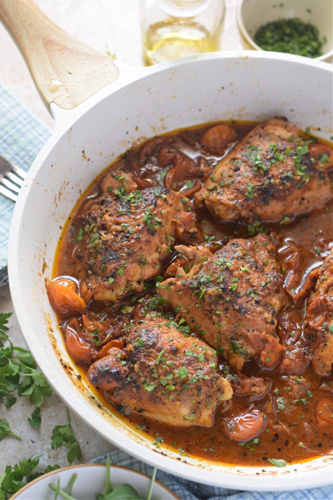 Chicken thighs cooked in a tomato sauce in a white skillet.