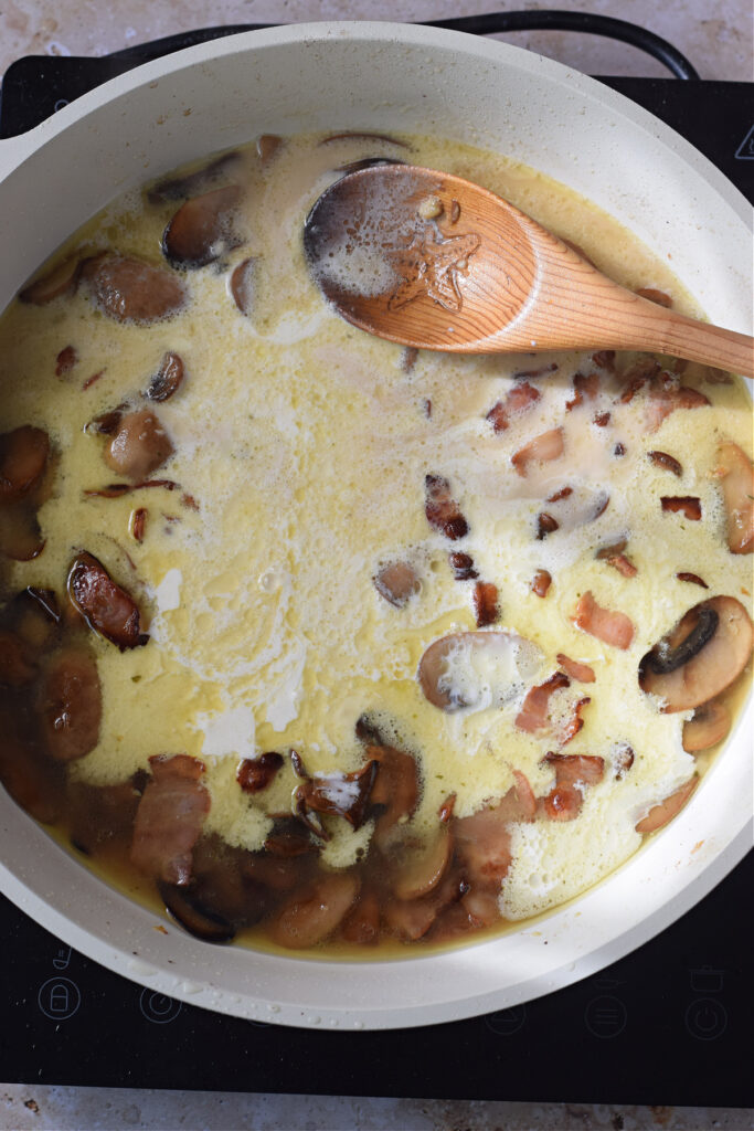 Adding heavy cream to a skillet with mushrooms and bacon.