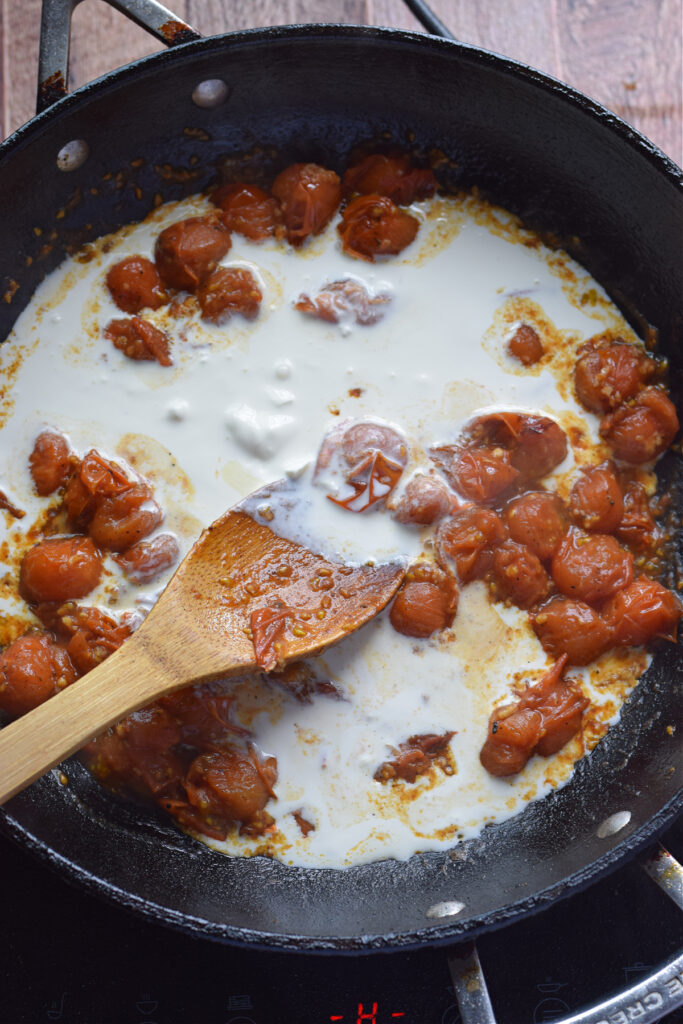 Adding cream to cherry tomatoes in a skillet.