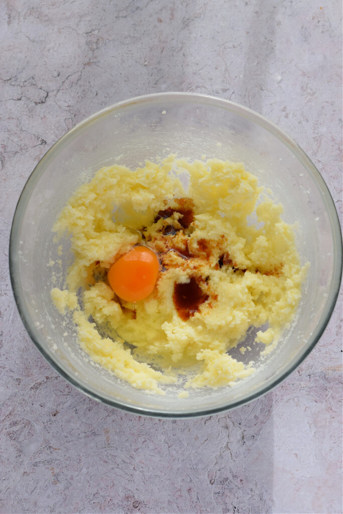 Adding an egg and vanilla extract to cookie dough.