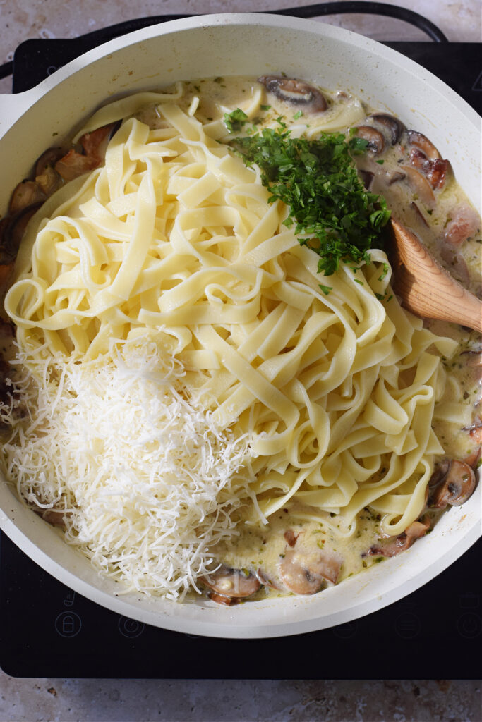 Adding tagliatelle, cheese and parsley to a skillet.
