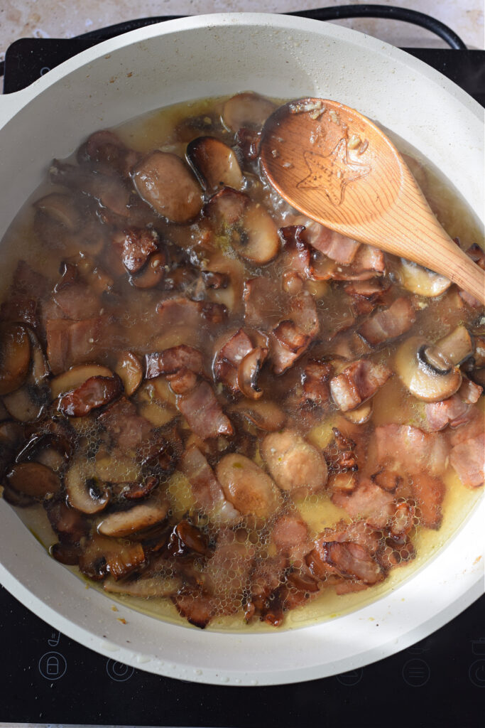 Adding vegetable broth to mushrooms and bacon in a skillet.
