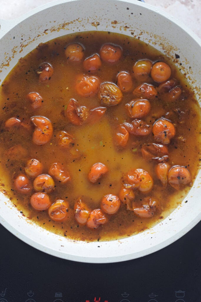 Tomatoes in vegetable broth in a white skillet.