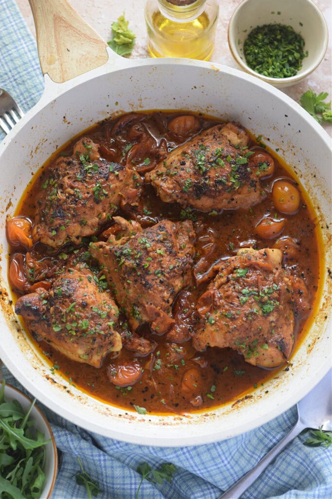 Chicken thighs cooked in a tomato sauce in a white skillet.