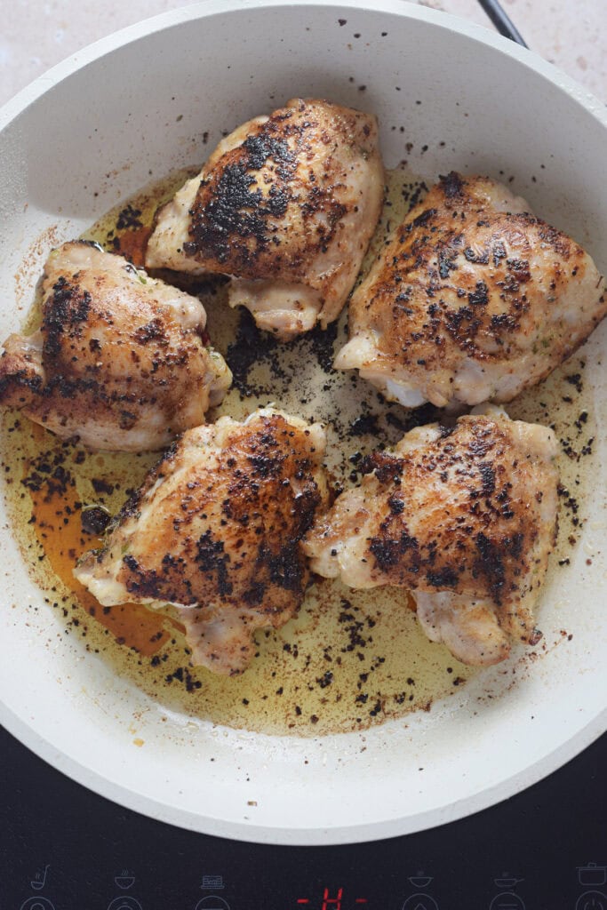 Browned chicken in a white skillet.