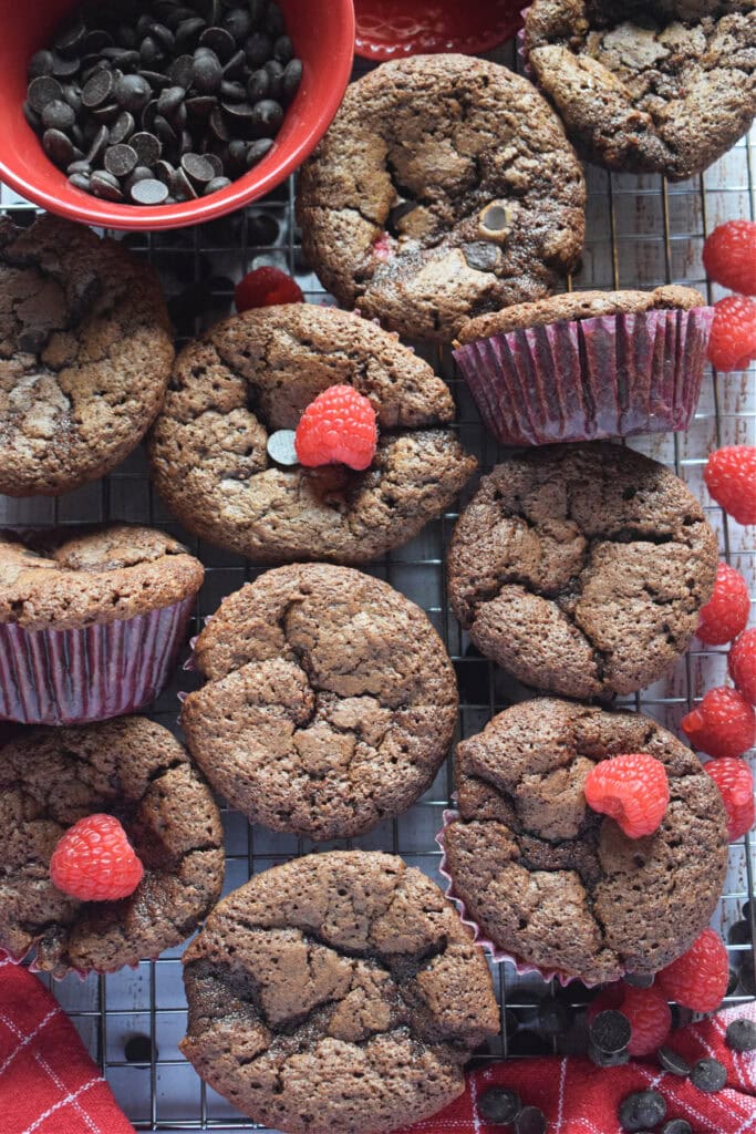 Chocolate muffins with raspberries on a cooling rack.