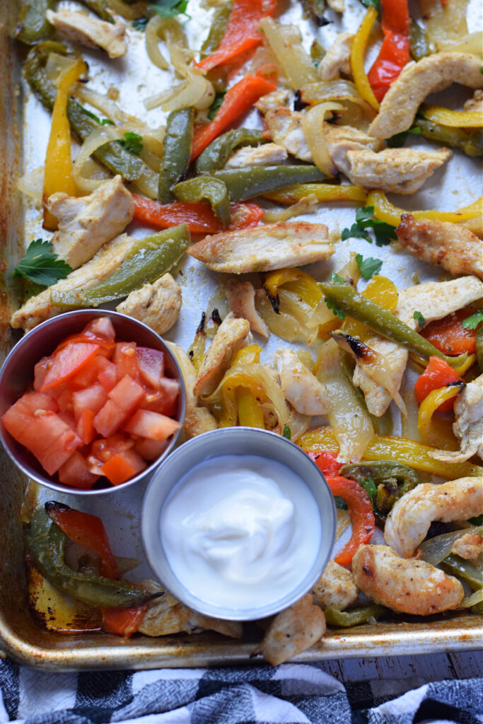 Chicken and peppers on a tray with a small dish of sour cream and tomatoes.