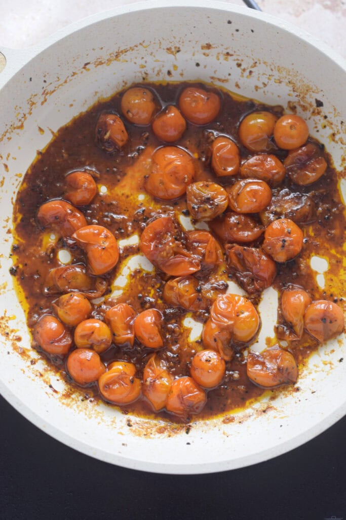 Cooked cherry tomatoes in a white skillet.