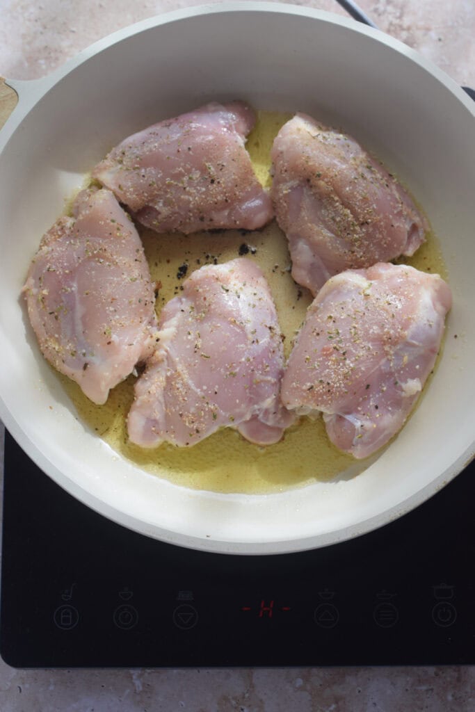 Chicken cooking in a white skillet.
