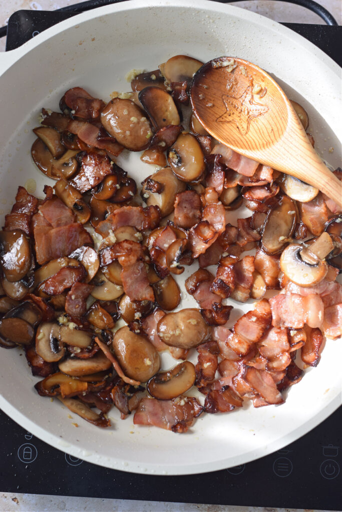 Cooking bacon and mushrooms in a skillet.