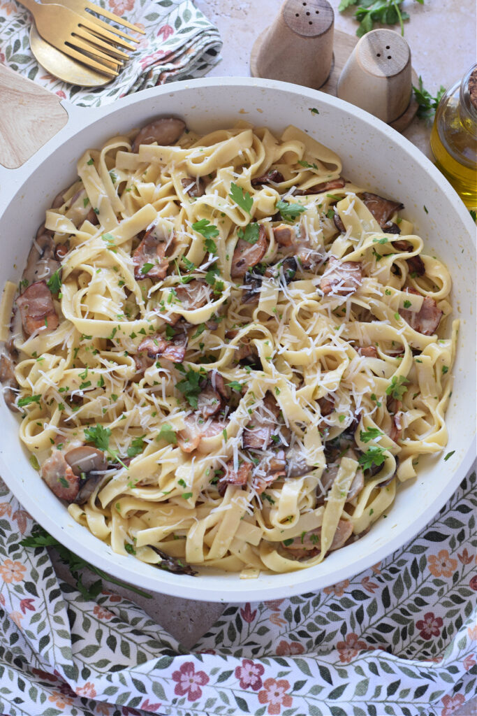 Creamy mushroom and bacon pasta in a white skillet.