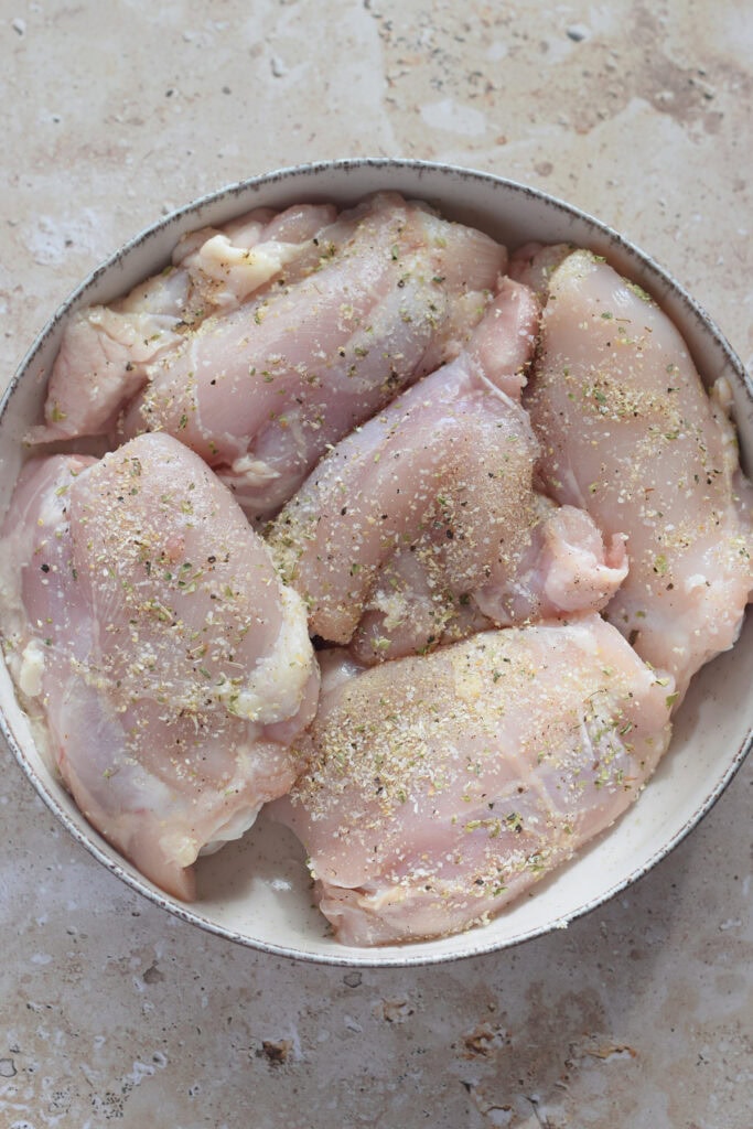 Seasoned uncooked chicken in a white bowl.