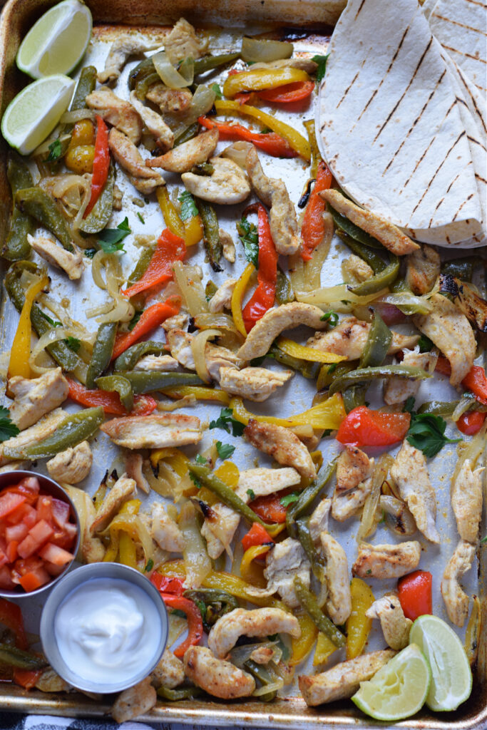 Sheet pan chicken and peppers on a tray with tortilla wraps.