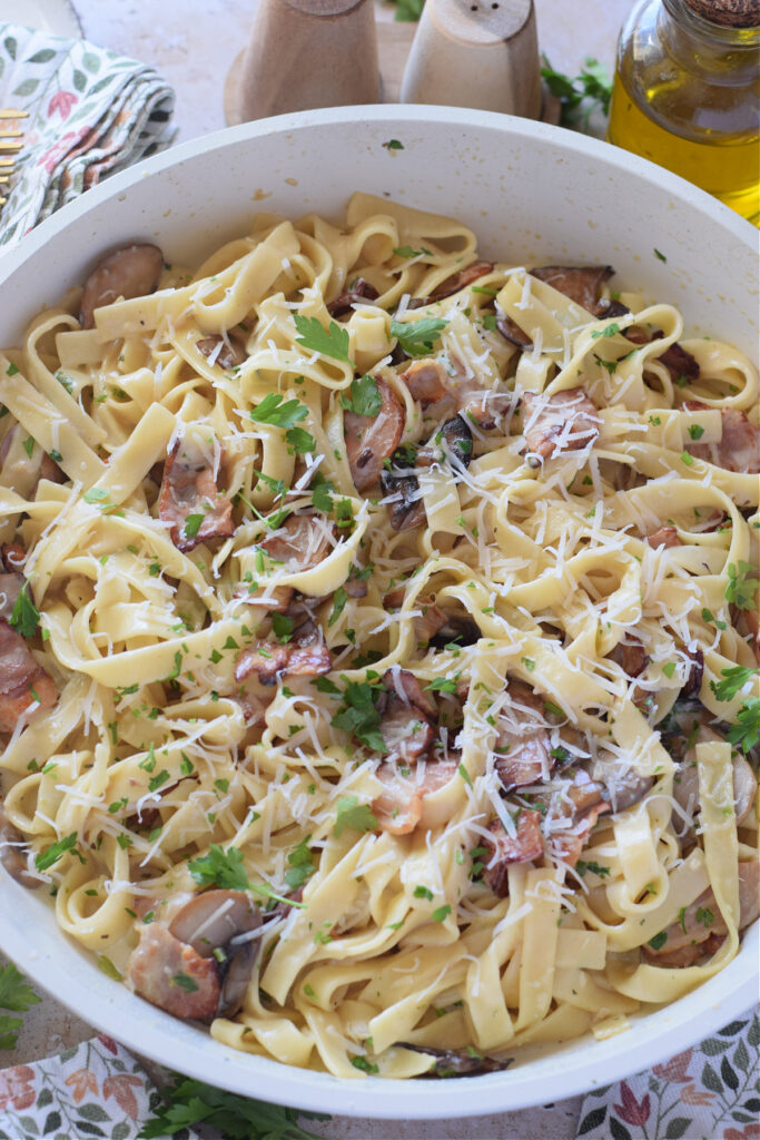 Tagliatelle pasta with bacon and mushroom in a white skillet.