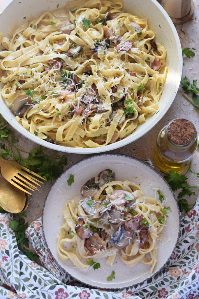 Creamy pasta with bacon and mushrooms in a white skillet.