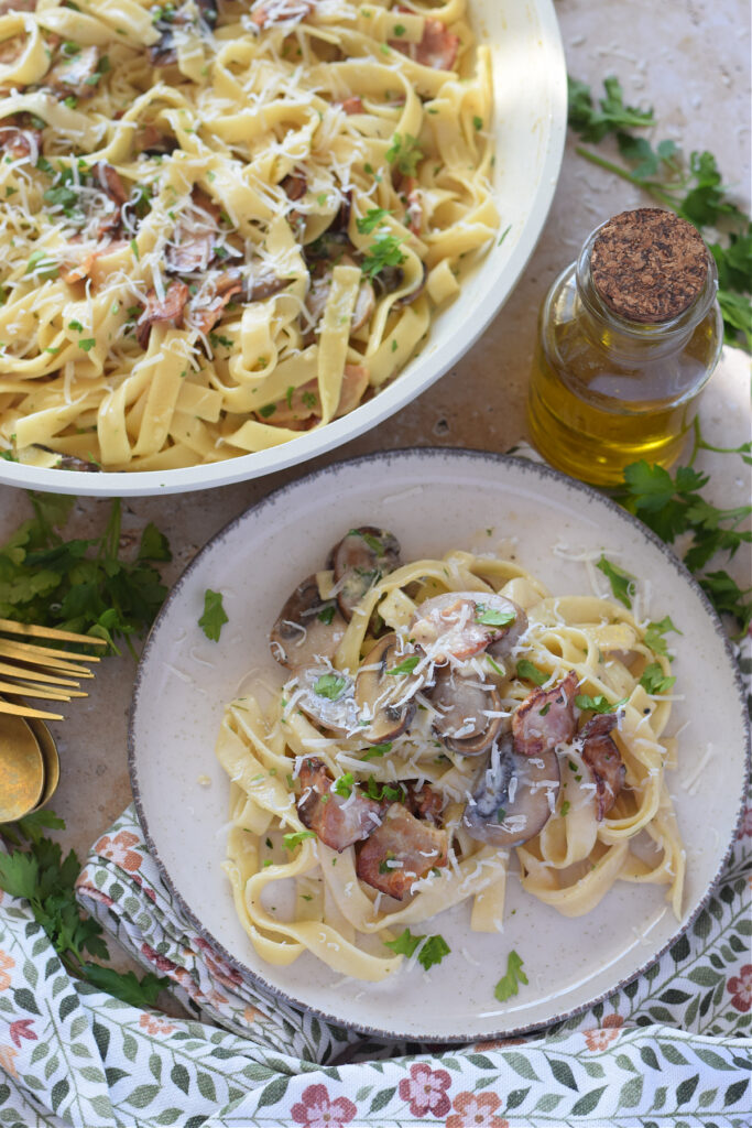 Pasta on a white plate with mushrooms and bacon.