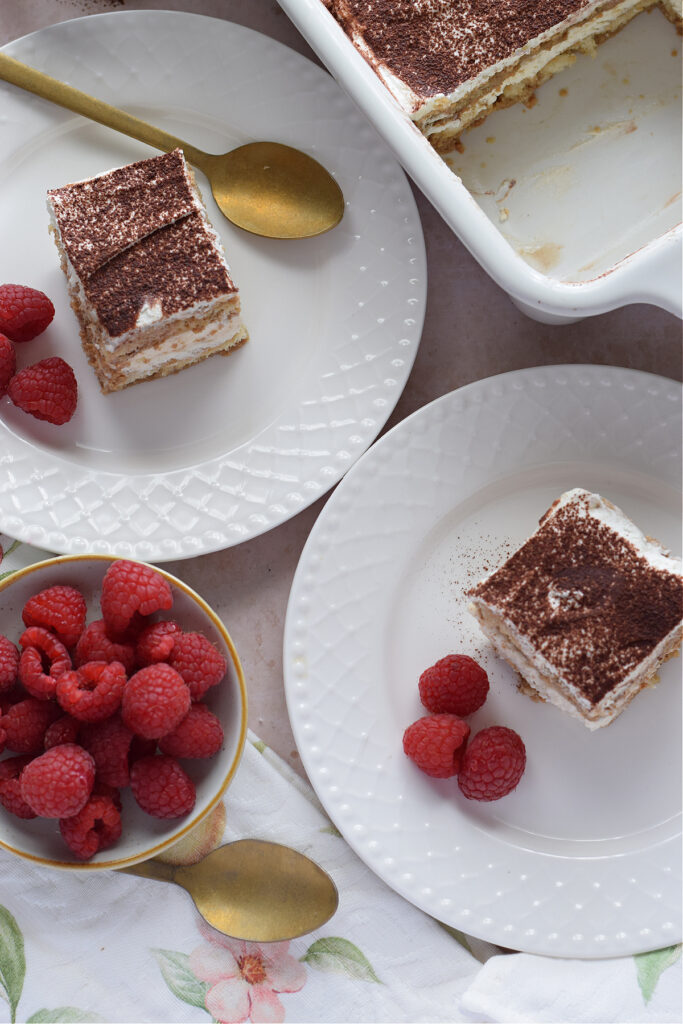 Tiramisu on white plates with raspberries.
