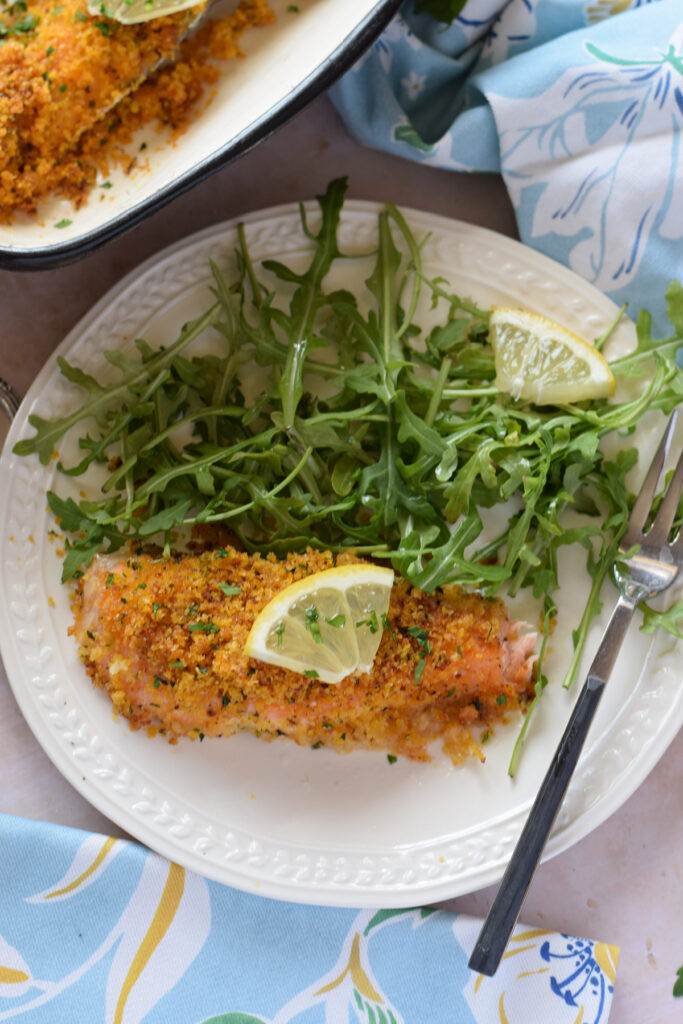Panko crusted salmon on a white plate with arugula salad leaves.