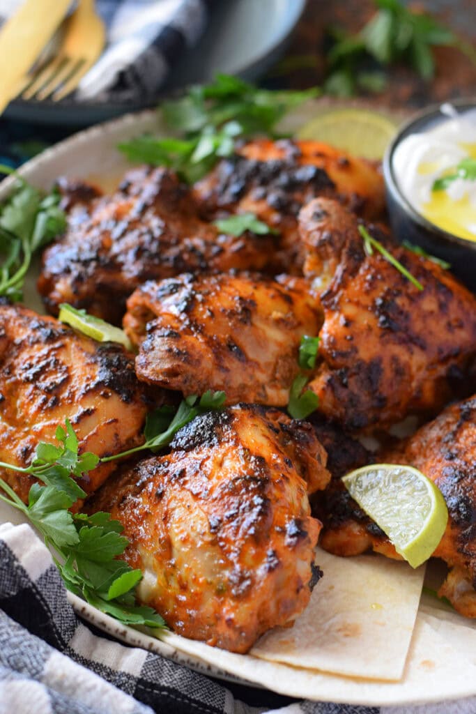 Close up of yogurt marinated chicken on a plate with lime pieces and parsley.