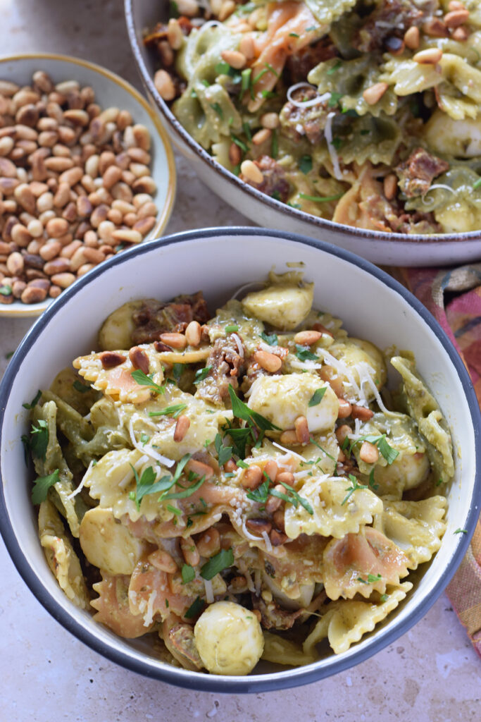 Close up of a green pesto pasta salad in a small white bowl.