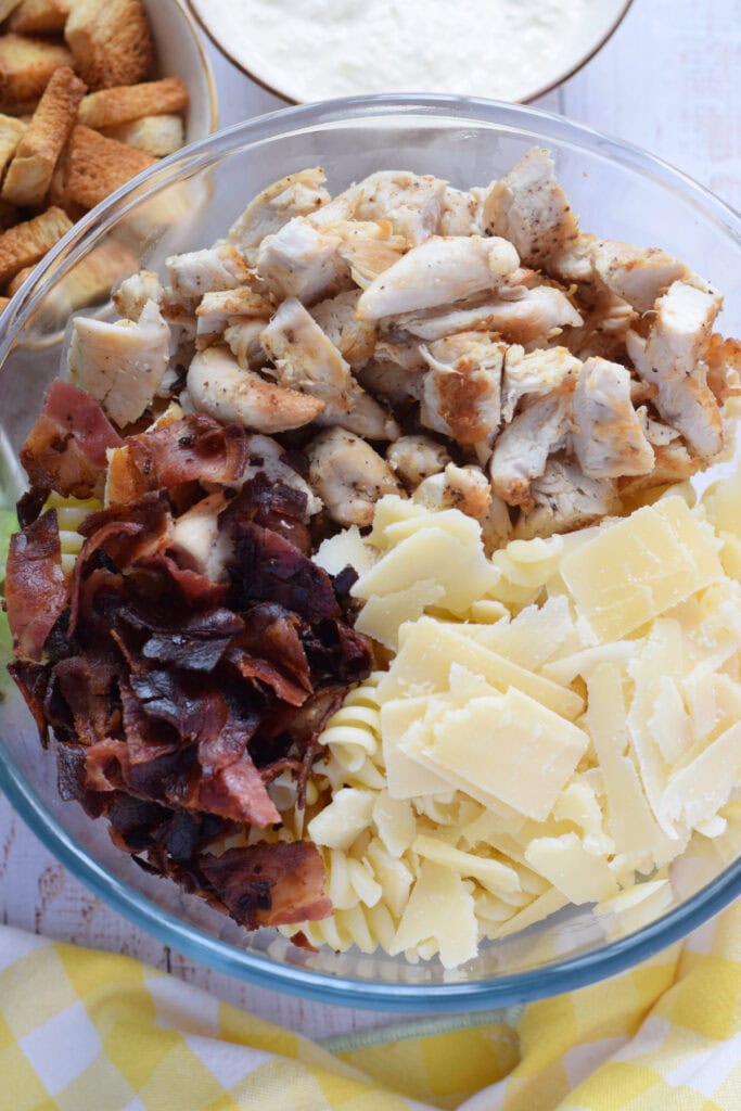 Making a chicken pasta salad in a glass bowl.