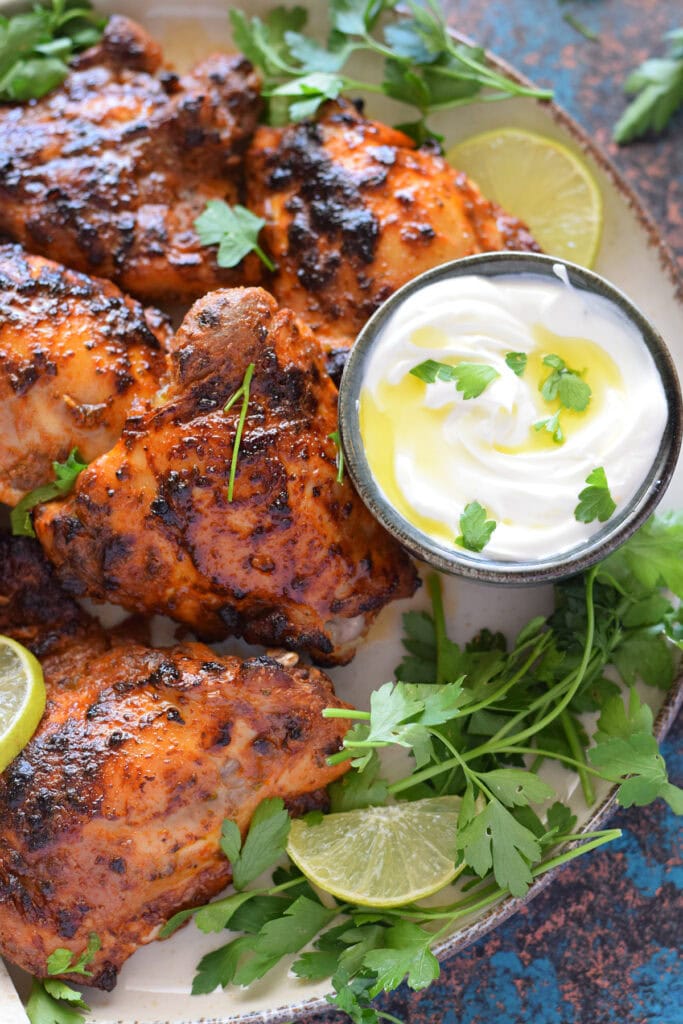 Close up of yogurt marinated chicken with a dip and parsley.