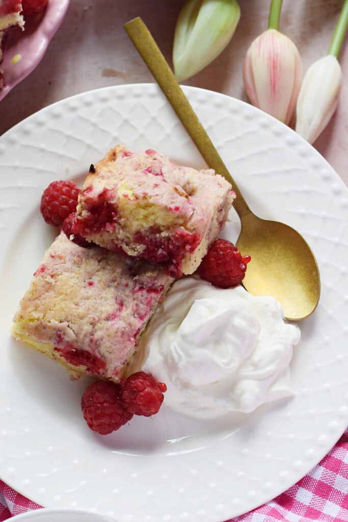 Cake squares with raspberries on a plate with cream.