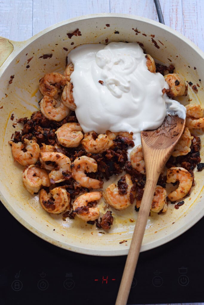 Adding cream to a skillet with sun dried tomatoes.
