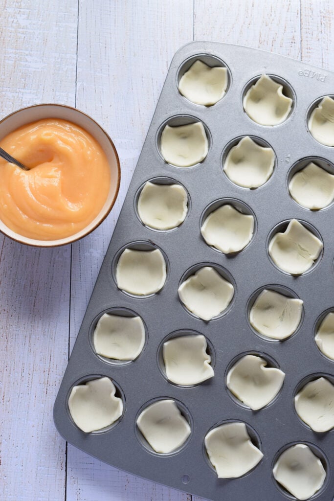 Lemon curd in a bowl and pastry squares in a muffin tin.