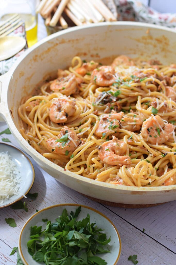 Shrimp pasta with sun dried tomatoes in a white skillet.