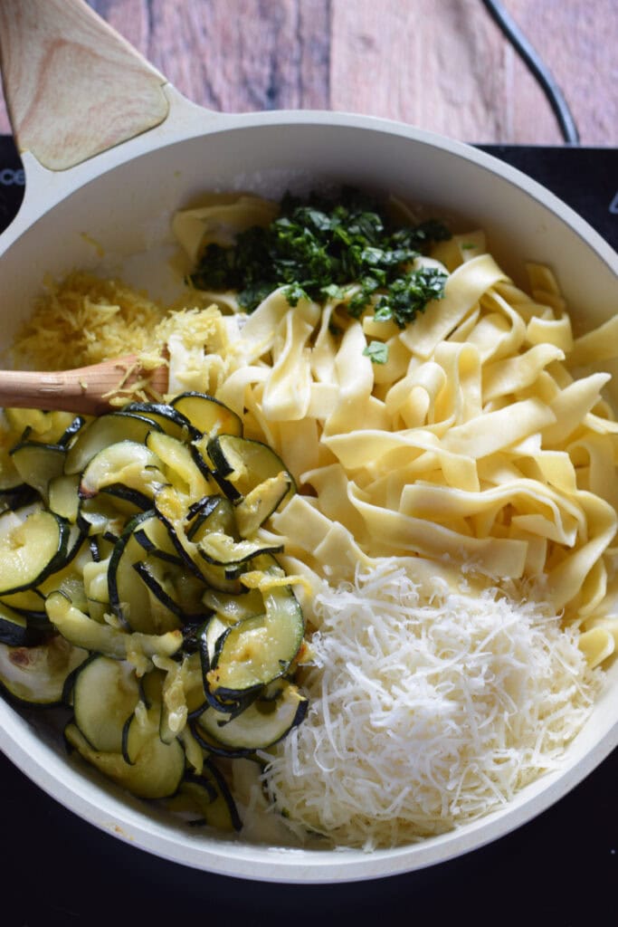 Adding ingredients to a white skillet to make a zucchini pasta dish.