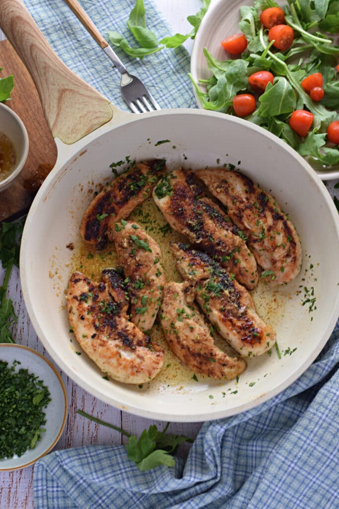 Chicken tenders in a white skillet.