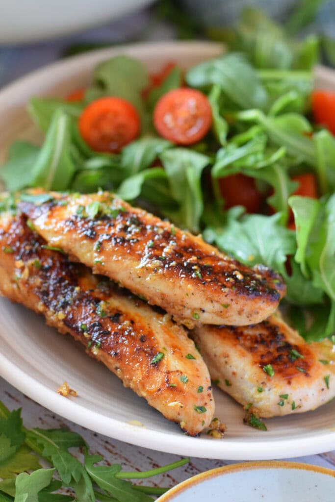 Close up of garlic butter chicken tenders with a salad.