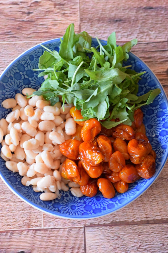 Combined cherry tomatoes, arugula and white beans in a blue bowl.