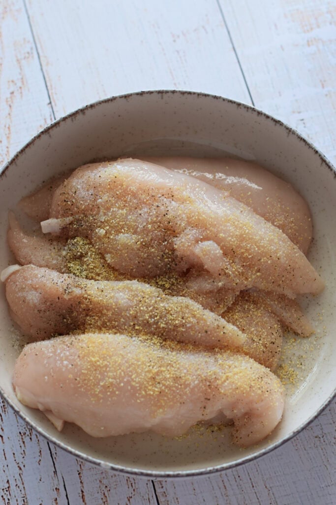 Chicken tenders coated with seasoning in a bowl.