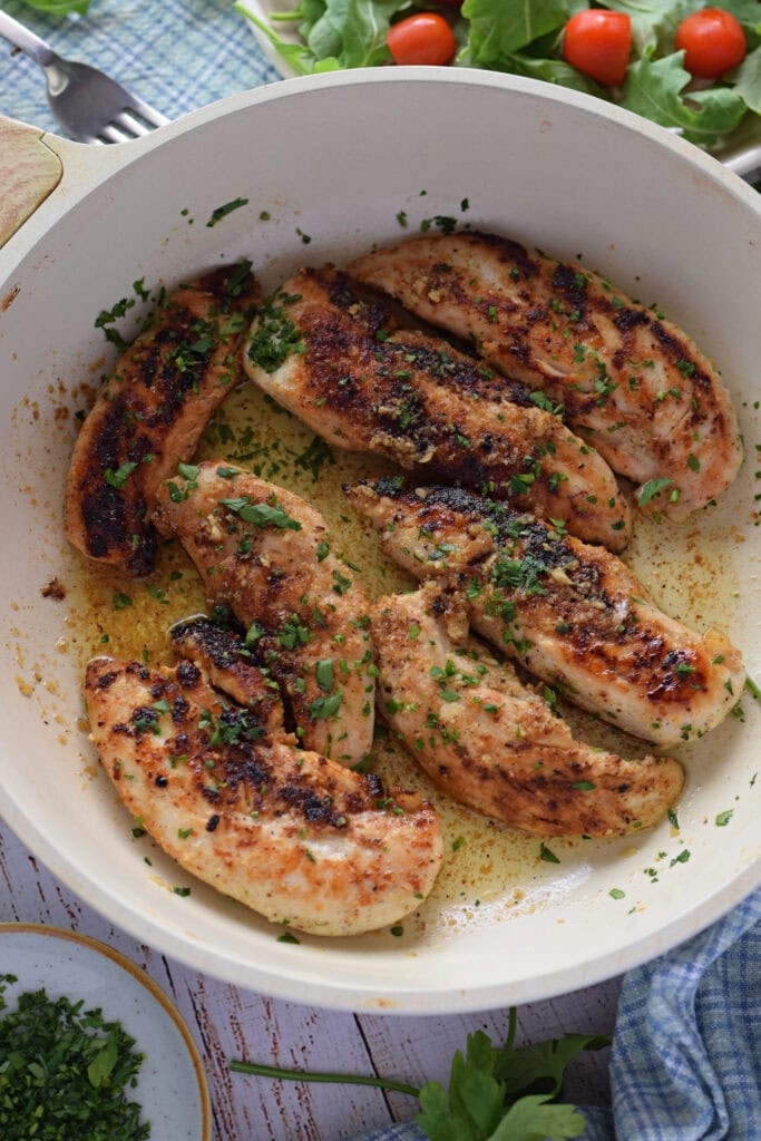 Chicken tenders with garlic butter in a skillet.