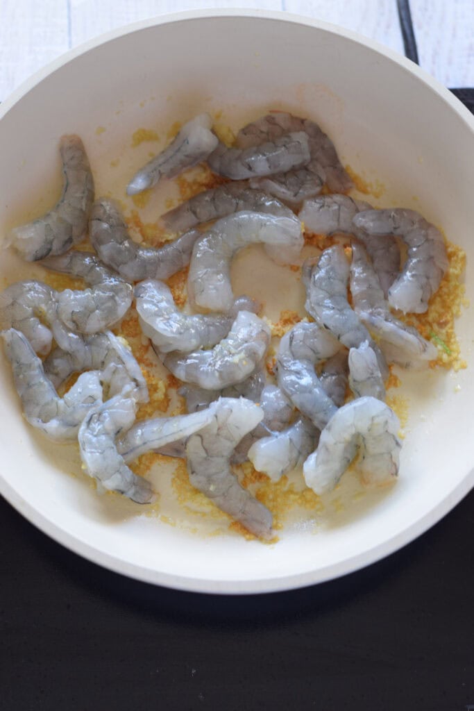 Adding shrimp in a white skillet.