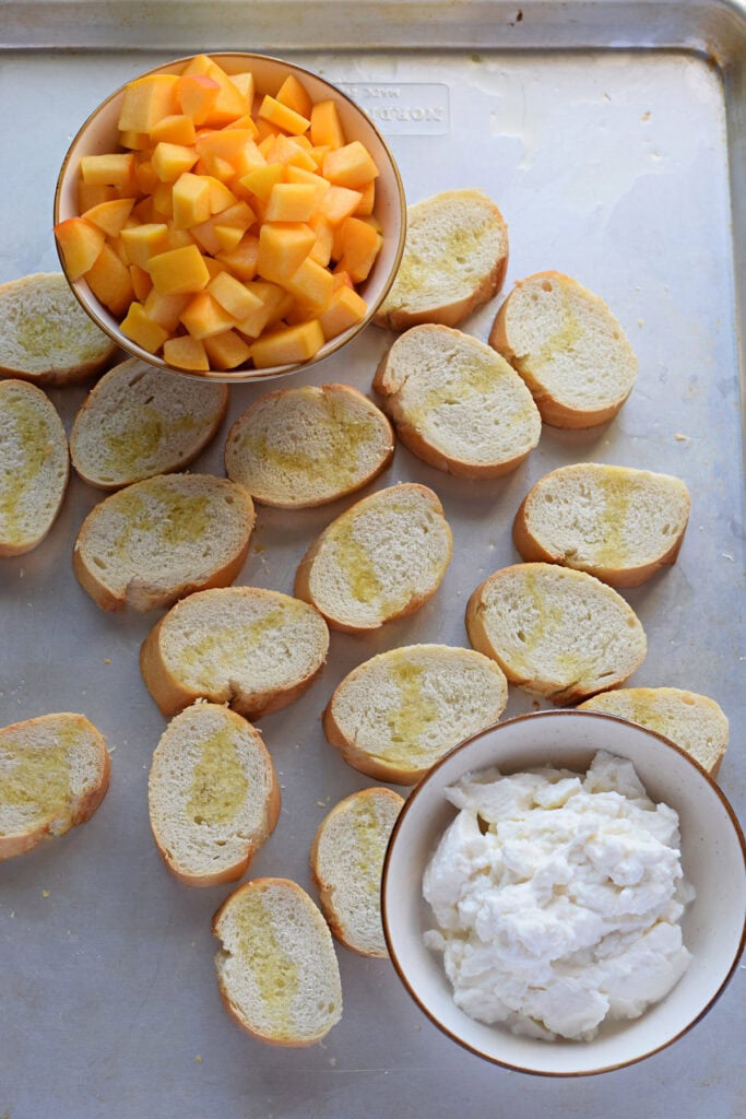 Baguette bread on a baknig tray with peaches and mascarpone cheese.